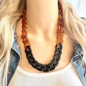 May include: A chunky chain necklace with a two-tone design. The top half of the necklace is made of amber-colored plastic, while the bottom half is black.