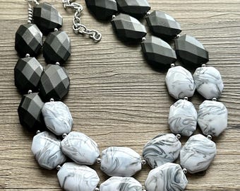 May include: A two-strand necklace with large, faceted black and white marble-patterned beads. The necklace is made of plastic and has a silver clasp.