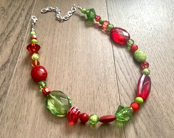 May include: A red and green beaded necklace with a silver chain. The necklace features various shapes and sizes of beads, including round, oval, and faceted.