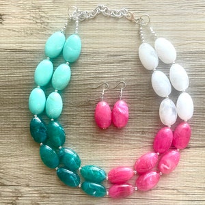 May include: A two-strand necklace with large oval beads in shades of teal, white, and pink. Matching earrings with pink oval beads are included.