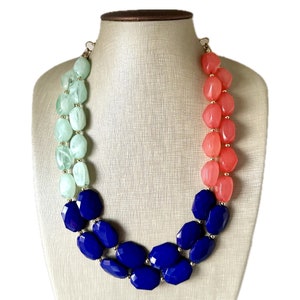 May include: A multi-strand necklace with large, graduated beads in shades of green, coral, and blue. The beads are faceted and have a glossy finish.