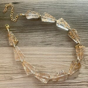 May include: A gold and clear glass necklace with a geometric design. The necklace is made of faceted glass beads with gold wire accents. The necklace is strung on a gold chain with a lobster clasp.