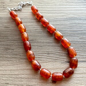 May include: A necklace made of amber beads. The beads are a rich orange colour and are strung on a silver chain.