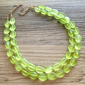 May include: A double strand necklace made of light green oval-shaped beads with a gold chain clasp.