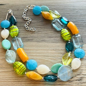 May include: A multi-strand necklace with large, colorful beads in shades of blue, green, yellow, and white. The beads are made of glass and have a variety of shapes and textures.
