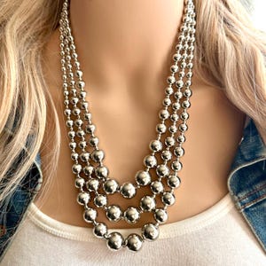 Puede incluir: Un collar de plata de múltiples hilos con grandes cuentas redondas.