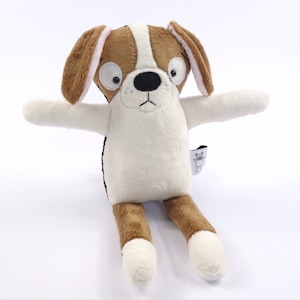 Op de afbeelding: Een bruin en wit pluche hondenspeelgoed met zwarte ogen en een zwarte neus. De hond zit met zijn armen uitgestrekt en heeft een wit label op zijn been met de tekst "Woof!"
