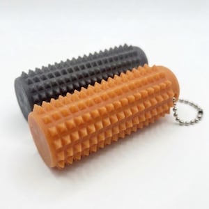 May include: Two cylindrical massage rollers with a textured, spiked surface. One roller is dark gray and the other is light orange. The orange roller features a small metal ball chain attached to one end, allowing it to function as a keychain.