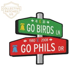 May include: An embroidered patch featuring two stacked street signs on a gray post. The top green sign reads GO BIRDS LN with a yellow bell icon and 41 E 33. The bottom red sign reads GO PHILS DR with a blue bell icon and 1980 E 2008.