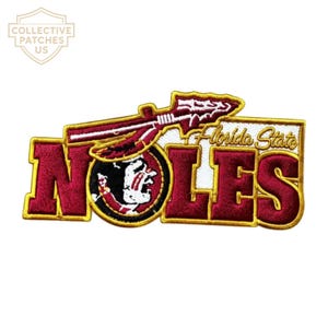 May include: An embroidered patch featuring the text NOLES in large maroon letters with gold trim. A spear graphic sits above the text, and a circular emblem depicting a profile of a person with face paint is integrated into the letter O.