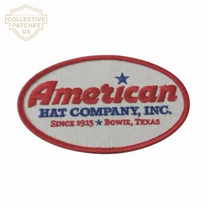 Peut inclure: Un écusson brodé de forme ovale avec un fond blanc et une bordure rouge. Il présente le texte rouge American, le texte bleu HAT COMPANY, INC. et le texte rouge SINCE 1915 BOWIE, TEXAS, accentué par deux petites étoiles bleues.