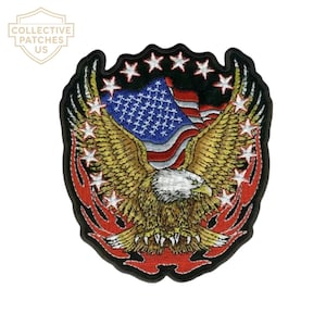 May include: An embroidered patch featuring a bald eagle with spread wings centered in front of a waving American flag. The design is framed by a black border with white stars and red flame-like accents along the bottom edges.