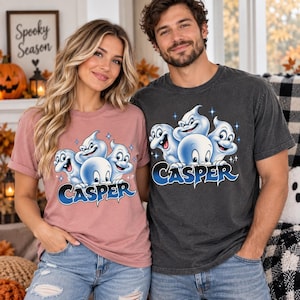 May include: A dusty rose t-shirt and a charcoal gray t-shirt, both featuring a graphic print of four cartoon Casper ghosts with blue and white highlights and the text "CASPER" in a bold, stylized blue font across the chest area of each shirt.