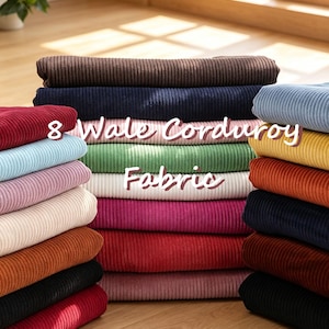 May include: A stack of folded 8 Wale Corduroy Fabric in various colours including brown, navy, light blue, yellow, green, white, pink, red, and black. The fabric features a distinct vertical ribbed texture throughout the entire collection.