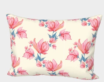Puede incluir: Cojín rectangular con fondo crema y un patrón repetido de flores rosas de acuarela con tallos y hojas azules. Las flores son de varios tamaños y arreglos.