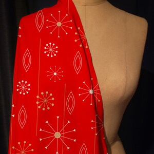May include: A vibrant red fabric with a mid-century modern design. The pattern features white and gold starbursts, vertical lines, and oval shapes. The fabric is draped over a vintage dress form.