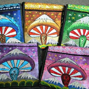 May include: Five colorful embroidered pouches with a mushroom design. Each pouch features a different color background and a mushroom with a white and red striped cap. The mushrooms are all surrounded by a mountain scene with white peaks and a starry night sky.
