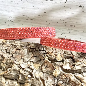 Puede incluir: Dos collares de perro de color rosa con pedrer&iacute;a sobre un trozo de madera.