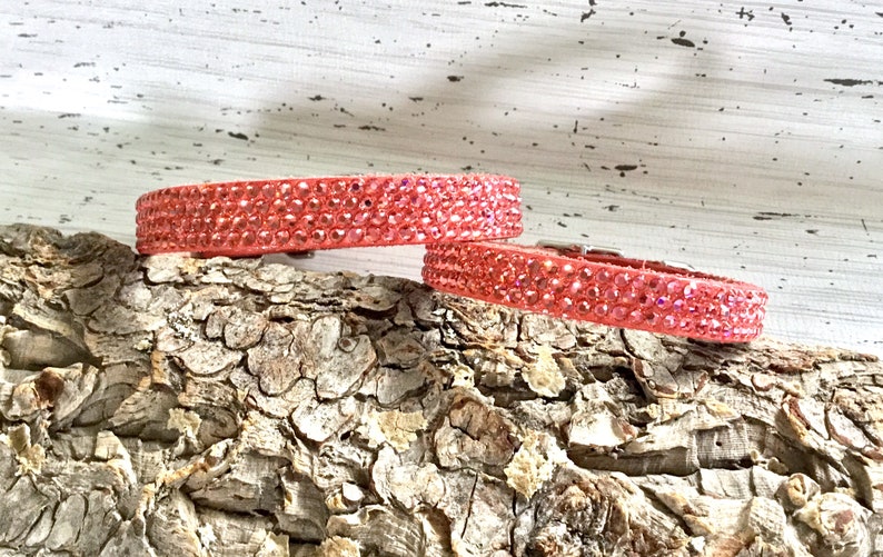 Puede incluir: Dos collares de perro de color rosa con pedrer&iacute;a sobre un trozo de madera.