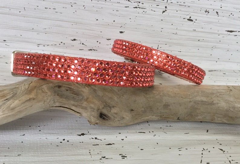 Puede incluir: Dos collares de perro de color coral con pedrer&iacute;a, uno m&aacute;s grande que el otro, est&aacute;n sobre un trozo de madera flotante.
