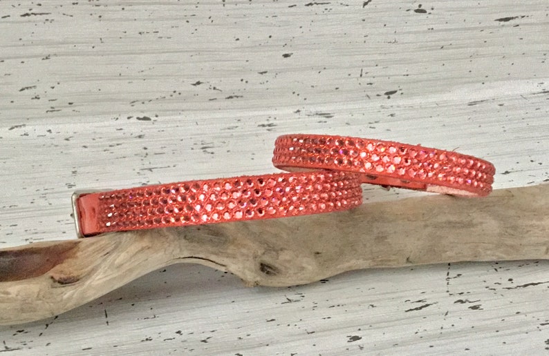 Puede incluir: Dos collares de cuero de color coral con filas de brillantes de imitaci&oacute;n. Los collares est&aacute;n sobre una superficie de madera clara.