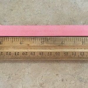 Puede incluir: Un collar de perro de cuero rosa con una hebilla plateada y cinco agujeros. El collar se mide con una regla, mostrando que tiene aproximadamente 25 cm de largo.