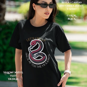 May include: A black Bella + Canvas 3001 unisex jersey t-shirt featuring a graphic of a red and black snake coiled into a circle. The text "LET'S CIRCLE BACK AFTER THE HOLIDAYS" is printed in yellow and white around the snake illustration.