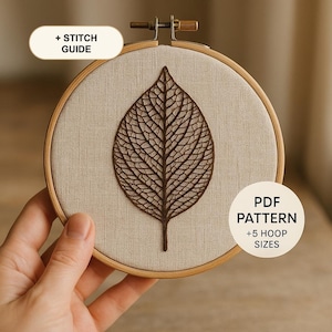 Könnte beinhalten: Ein runder Stickrahmen aus Holz mit beigem Stoff und einem dunkelbraun gestickten Blattskelett-Motiv. Die Textetiketten lauten + STITCH GUIDE und PDF PATTERN + 5 HOOP SIZES. Der Rahmen hat oben eine mittige Metallschraube zur Spannung.