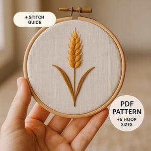 Puede incluir: Un bastidor de bordado que contiene tela blanca con un diseño de tallo de trigo amarillo dorado bordado en el centro. El bastidor cuenta con un tornillo de tensión de metal en la parte superior. Los textos superpuestos dicen + STITCH GUIDE y PDF PATTERN +5 HOOP SIZES.