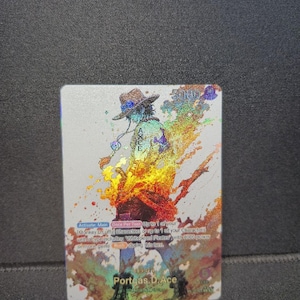 May include: A rectangular trading card featuring a holographic illustration of the character Portgas D. Ace from One Piece. The character wears a hat and is surrounded by vibrant, rainbow-colored flame effects. Text on the card includes game rules.