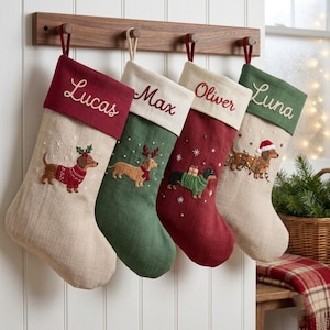 May include: Four personalised Christmas stockings hanging on a wooden rack. Each stocking features an embroidered dachshund dog and a name: Lucas, Max, Oliver, or Luna. The stockings are made of tan, green, and red fabric with festive details.
