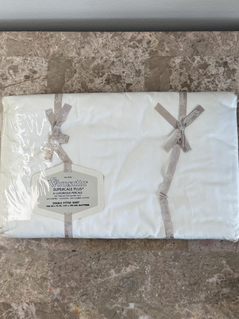 Puede incluir: Una s&aacute;bana bajera doble blanca Wamsutta Supercale Plus empaquetada en pl&aacute;stico transparente con cintas de marca. La etiqueta especifica 200 hilos por pulgada cuadrada, 50% poli&eacute;ster Fortrel y 50% algod&oacute;n peinado, para un colch&oacute;n de 137 x 190 cm.