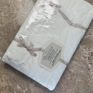 Puede incluir: Una s&aacute;bana bajera doble Wamsutta Supercale Plus blanca empaquetada en pl&aacute;stico transparente con una cinta de marca. La etiqueta especifica 200 hilos, 50% poli&eacute;ster y 50% algod&oacute;n peinado, para un colch&oacute;n de 137 x 190 cm.