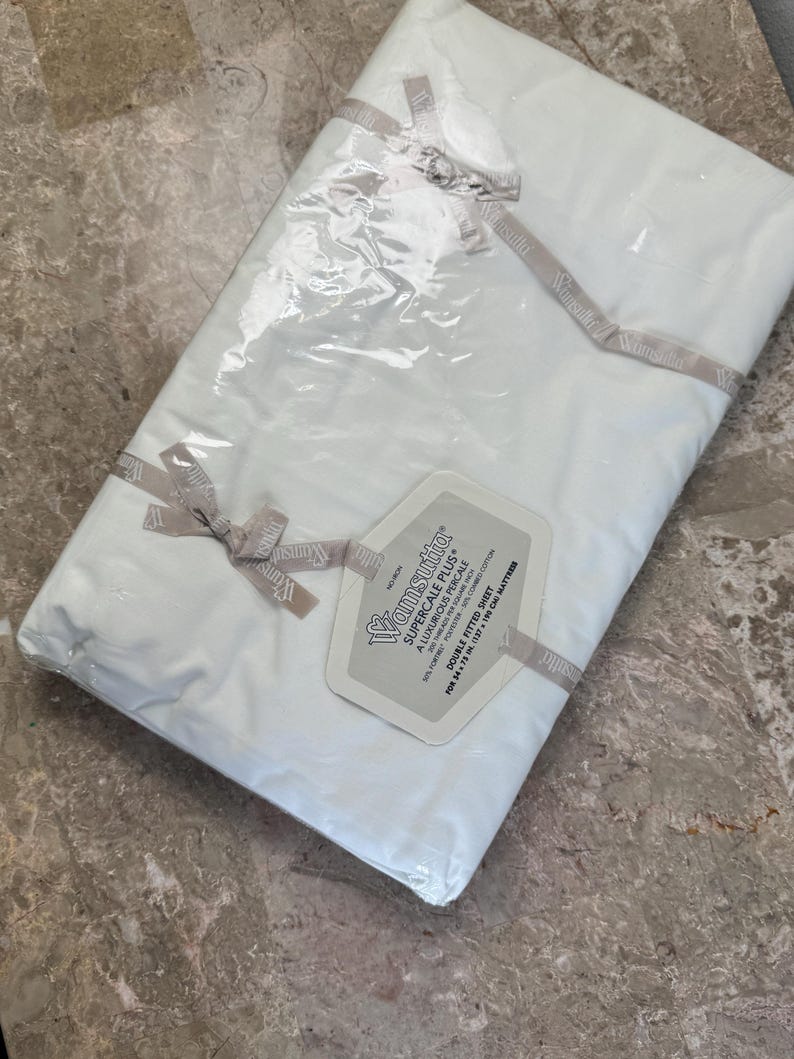 Puede incluir: Una s&aacute;bana bajera doble Wamsutta Supercale Plus blanca empaquetada en pl&aacute;stico transparente con una cinta de marca. La etiqueta especifica 200 hilos, 50% poli&eacute;ster y 50% algod&oacute;n peinado, para un colch&oacute;n de 137 x 190 cm.