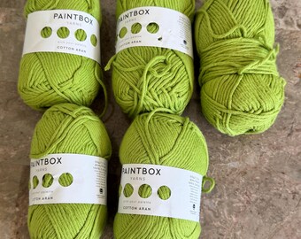 Puede incluir: Cinco ovillos de hilo Paintbox Yarns Cotton Aran de color verde lima. Cada ovillo tiene una etiqueta de papel blanco con el nombre de la marca, el texto 'pick your palette' y 'Cotton Aran'. El hilo es de color verde brillante sólido.