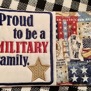 May include: A white pillow with blue and red embroidery that reads "Proud to be a MILITARY Family." A gold star is embroidered on the pillow. The back of the pillow is a patchwork of red, white, and blue fabric with a Statue of Liberty design.