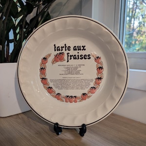 May include: A white ceramic pie dish with a fluted rim and a brown rim accent. The centre features the text "tarte aux fraises" in brown, surrounded by a circular illustration of strawberries and a printed French recipe for strawberry tart.