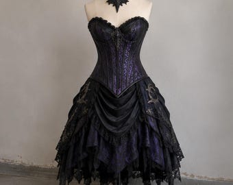 Puede incluir: Un vestido corsé negro y morado sin tirantes con escote corazón, falda de capas con ribete de encaje y gargantilla negra a juego. El corpiño muestra una tela estampada de color morado oscuro cubierta con material negro y adornos.