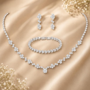 May include: A silver-toned jewellery set consisting of a necklace, a bracelet, and a pair of stud earrings. Each piece features a series of clear, round-cut stones arranged in a cluster pattern, connected by a delicate metallic chain link design.