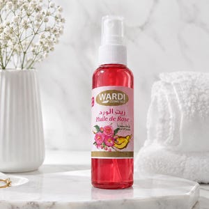 Peut inclure: Un flacon pulvérisateur en plastique transparent rempli d'huile de rose rouge. L'étiquette porte le texte Wardi Cosmetics, Huile de Rose et des caractères arabes, avec une illustration de roses roses et d'un pétale jaune. Bouchon blanc.