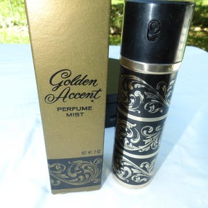 May include: A Golden Accent perfume mist spray bottle and its matching rectangular box. The bottle is black with gold filigree patterns and a black cap. The gold box features the text Golden Accent PERFUME MIST and NET WT. 2 OZ.