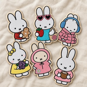 May include: Six embroidered patches featuring the white rabbit character Miffy in various outfits: holding a gingerbread cookie, wearing heart-shaped sunglasses with a strawberry, in a pink puffer coat, with a yellow bow, in a pink hoodie, and holding a mug.