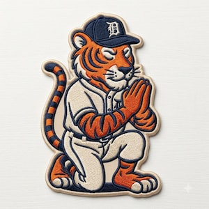 May include: An embroidered patch featuring an orange and black tiger wearing a navy blue baseball cap with a white letter D and a matching baseball uniform. The tiger is kneeling with its hands pressed together in a prayer-like gesture.