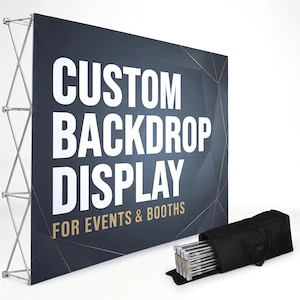 May include: A large rectangular backdrop display with a dark blue background and white text reading CUSTOM BACKDROP DISPLAY FOR EVENTS & BOOTHS. The display is supported by a silver metal accordion-style frame and includes a black carrying bag.