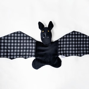May include: A plush bat toy with a black body and wings. The wings are patterned with a black and gray gingham design. The bat has yellow eyes and a small white tag.