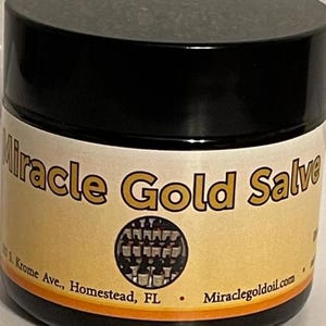 Könnte beinhalten: Ein zylindrischer Tiegel mit schwarzem Schraubdeckel und beigem Etikett. Das Etikett zeigt den Text Miracle Gold Salve in Fettdruck, eine kreisförmige Grafik mit kleinen Flaschen sowie die Adresse 303 S. Krome Ave., Homestead, FL, und die Website.