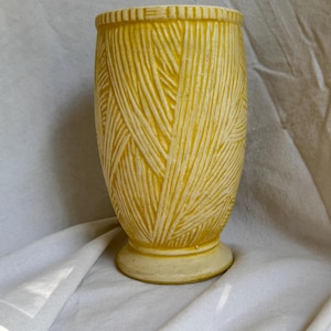 May include: A bright yellow ceramic vase featuring a textured, raised pattern of diagonal lines across its cylindrical body. The vase has a flared rim with vertical notches and a circular base, showcasing a matte finish with subtle white highlights.