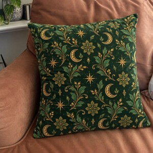 Puede incluir: Un cojín cuadrado con una base de tela verde oscuro que presenta un patrón repetitivo de lunas crecientes doradas, estrellas de ocho puntas y motivos florales estilizados con hojas verde claro y tallos dorados en todo el diseño.