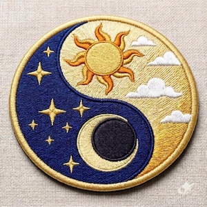 May include: A circular embroidered patch featuring a yin-yang design. One side is dark blue with gold stars and a crescent moon. The other side is golden yellow with a bright sun and white clouds. The entire patch has a thick gold border.