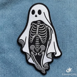 May include: An embroidered patch featuring a white ghost sheet draped over a grey human skeleton torso. The design is outlined in black thread and set against a black background, creating a high-contrast graphic of a skeletal figure.